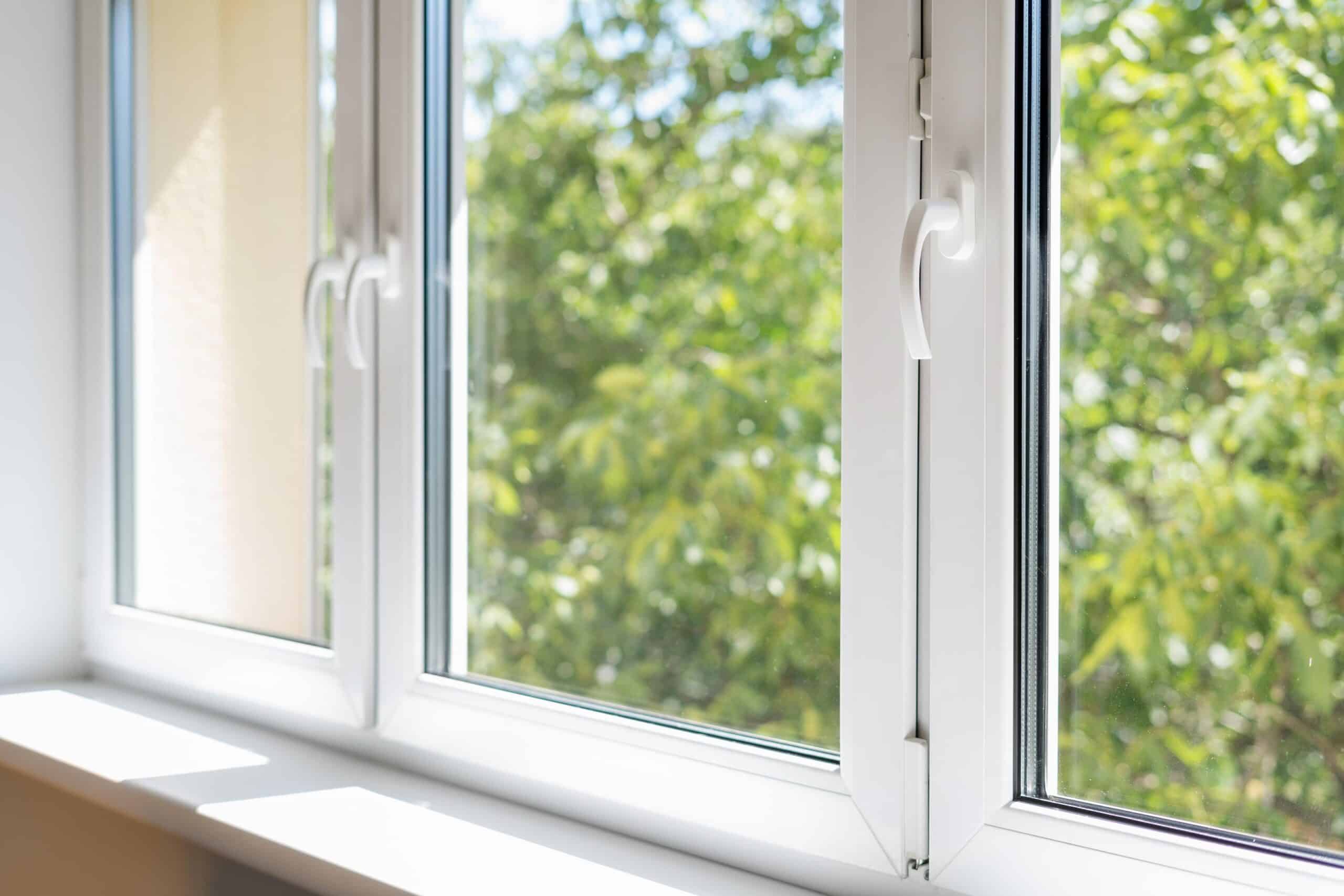 Modern white PVC window with double glazing and a view of green trees outside.