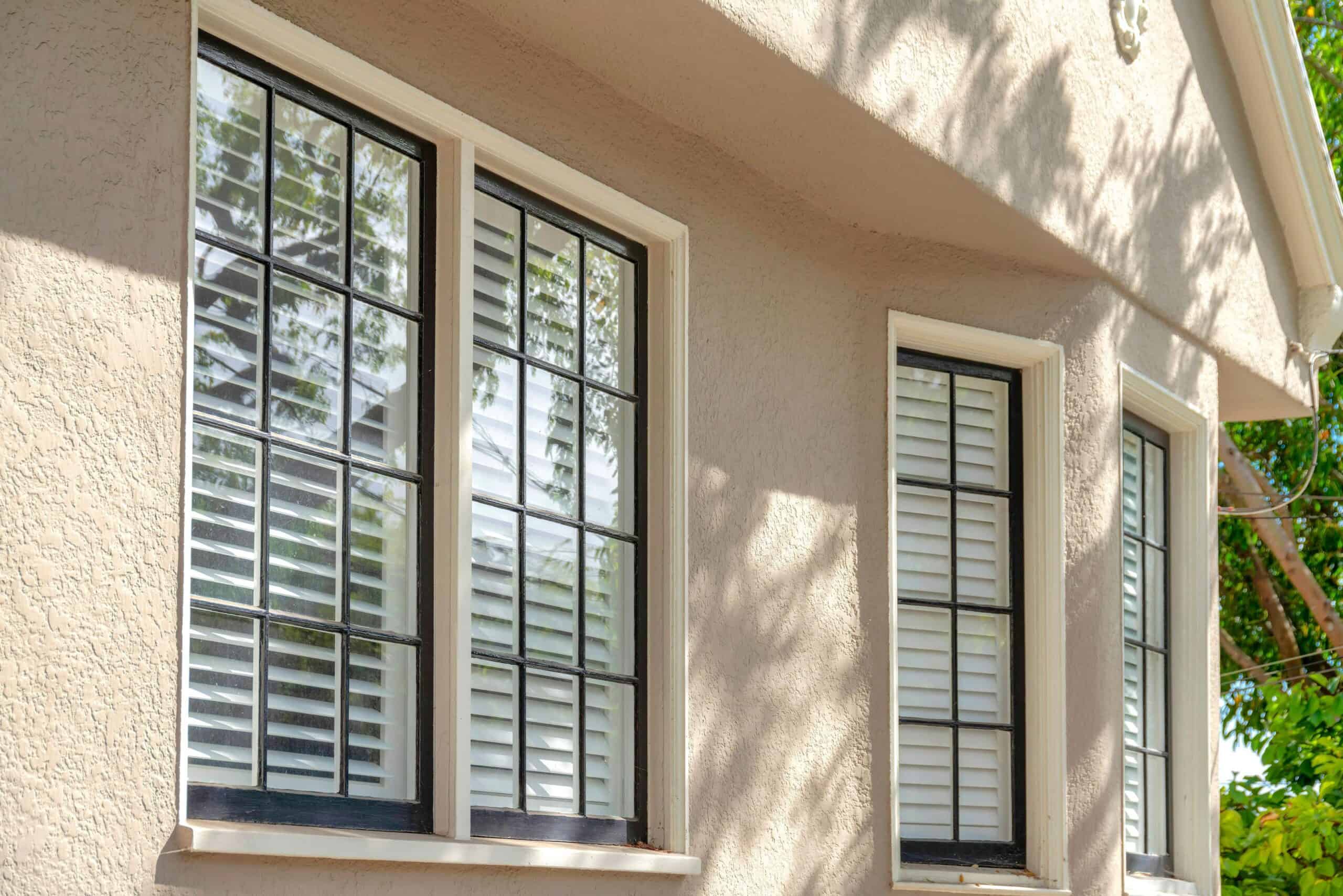 Modern double-hung windows with white frames and shutters on a beige house exterior.