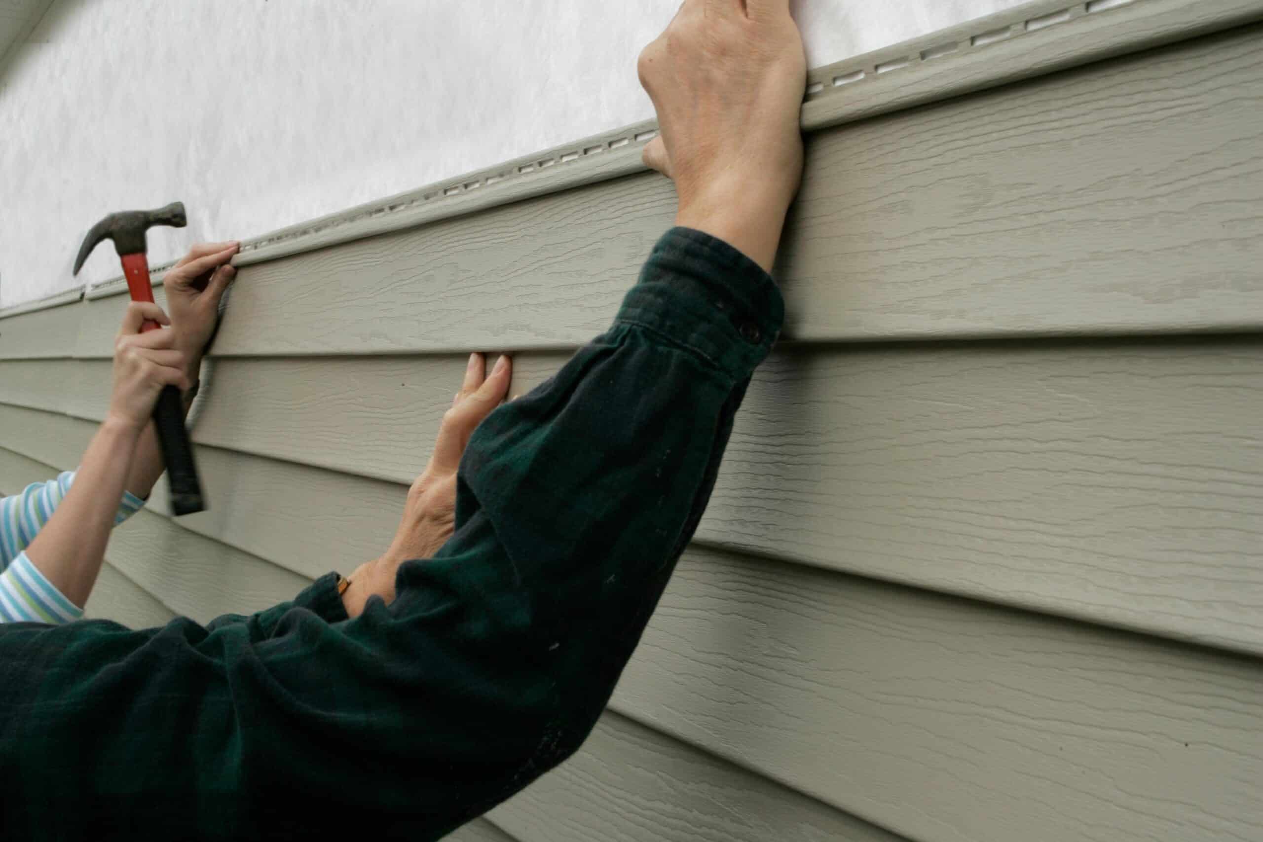 Workers installing vinyl siding on a house exterior for improved insulation and aesthetics.