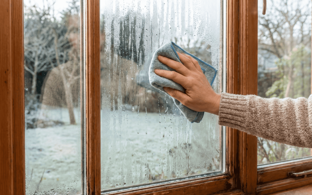 Person cleaning a wooden window with a cloth and spray on a rainy day.