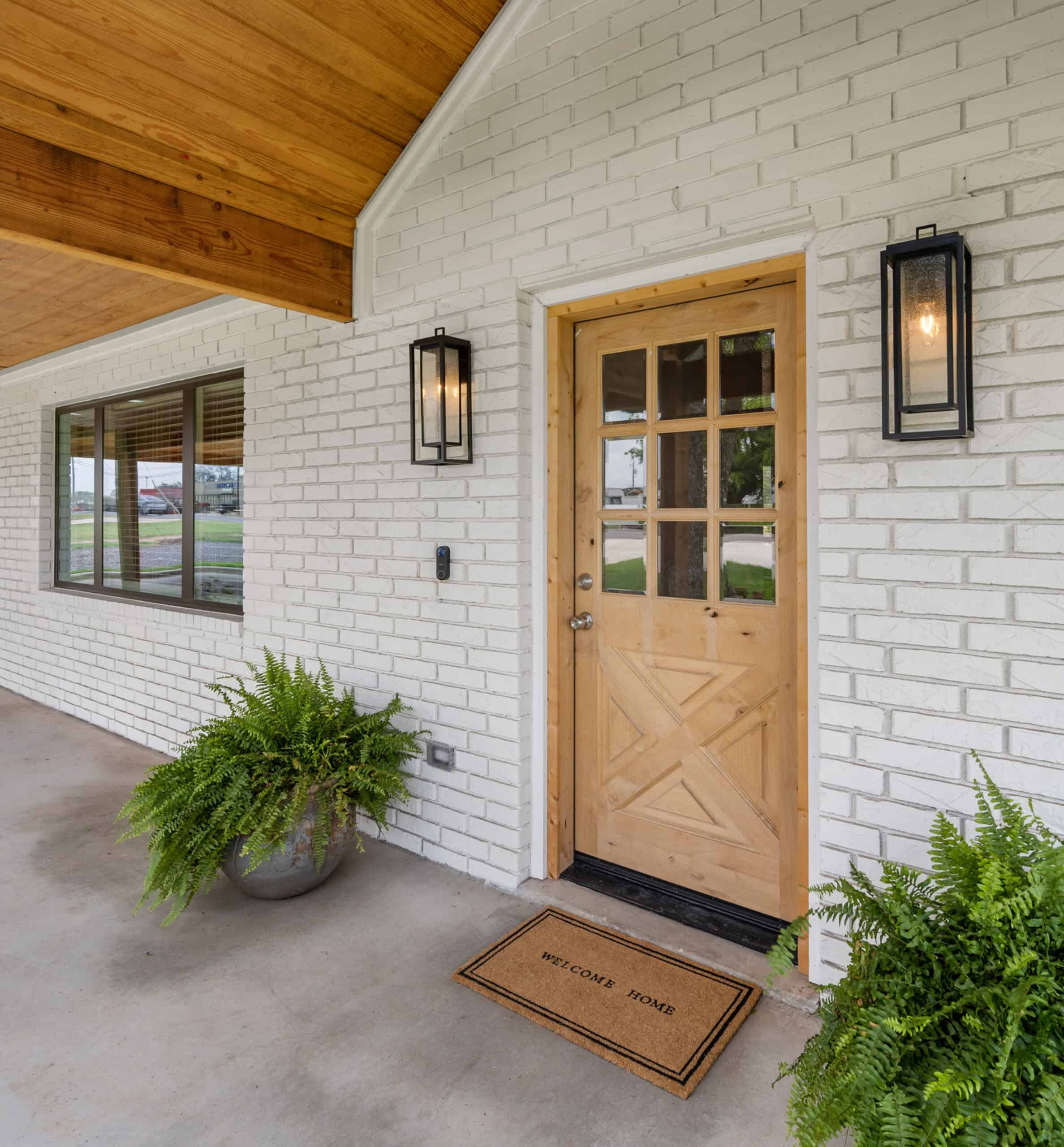 Beautiful wooden front door with glass panels and black wall-mounted lanterns, enhancing curb appeal.