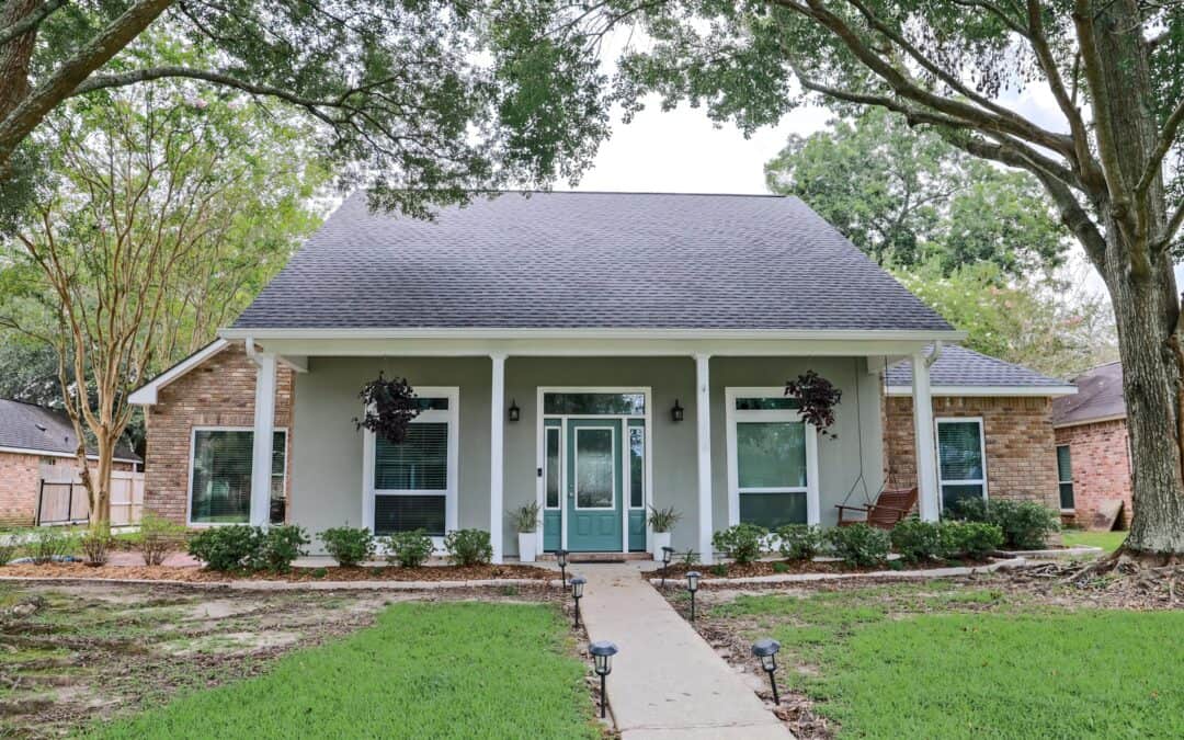 Beautiful house with large windows and a front porch, surrounded by trees and greenery.