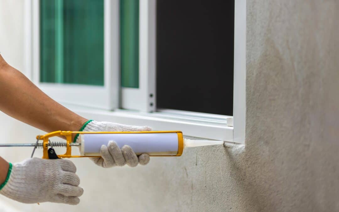 Worker applying sealant to window frame for insulation and weatherproofing.