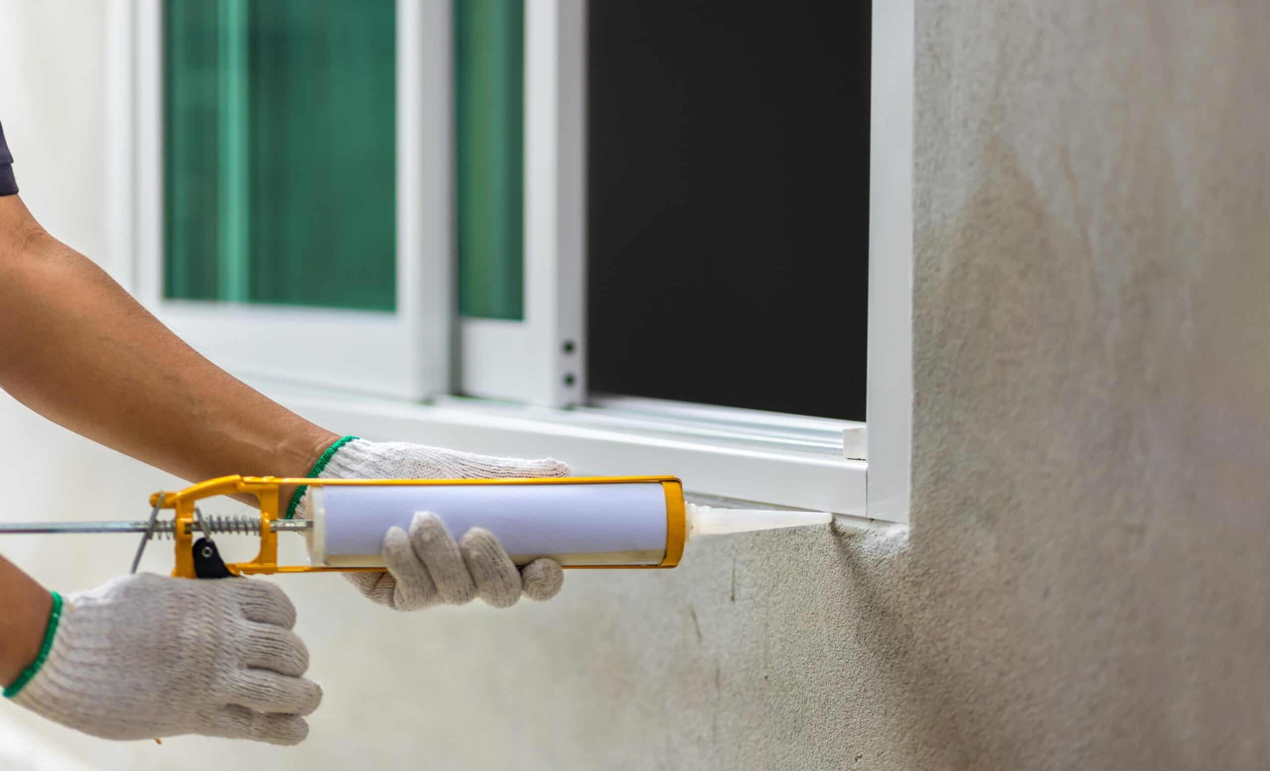 Worker applying sealant to window frame for insulation and weatherproofing.