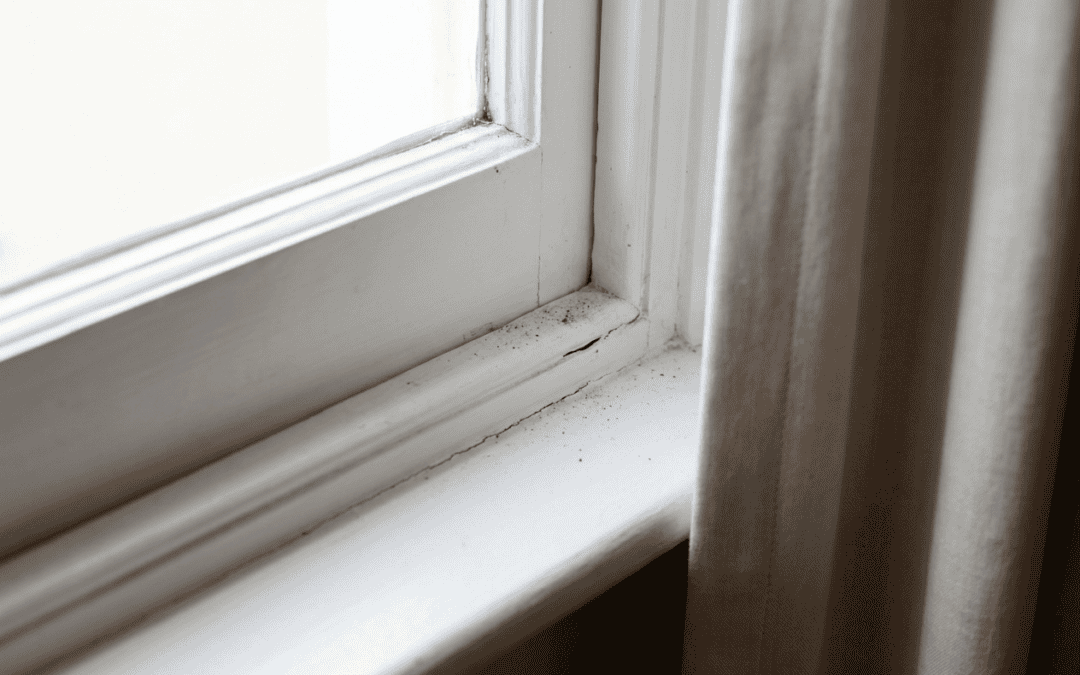 Close-up of a white window frame with a beige curtain beside it, showing some dust and dirt on the s.