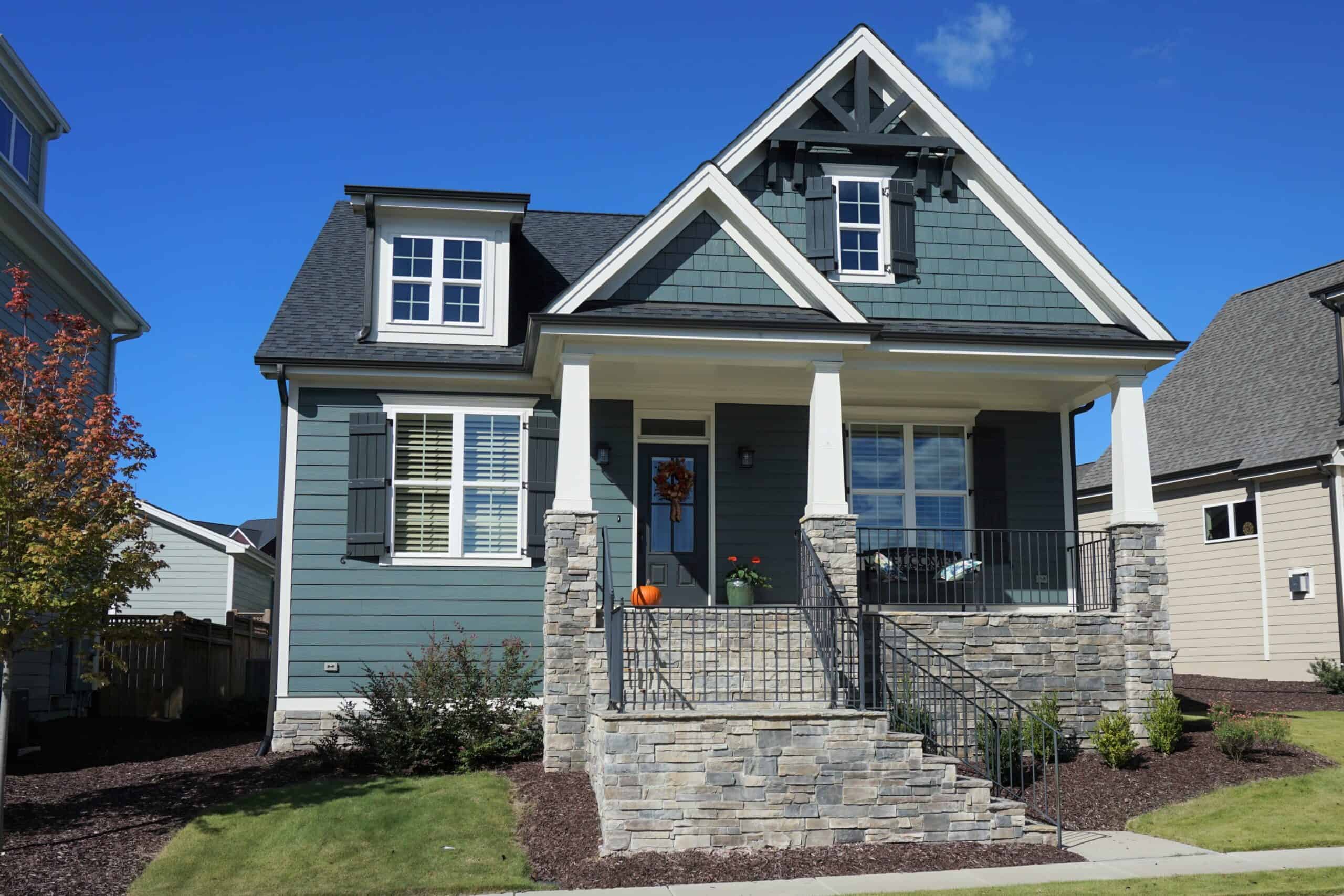 Modern blue house with white trim, stone steps, and front porch under a clear blue sky.